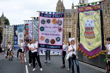 Artist Lucy Orta, London College of Fashion students and staff hold five of the banners outside the houses of parliament on an empty road.