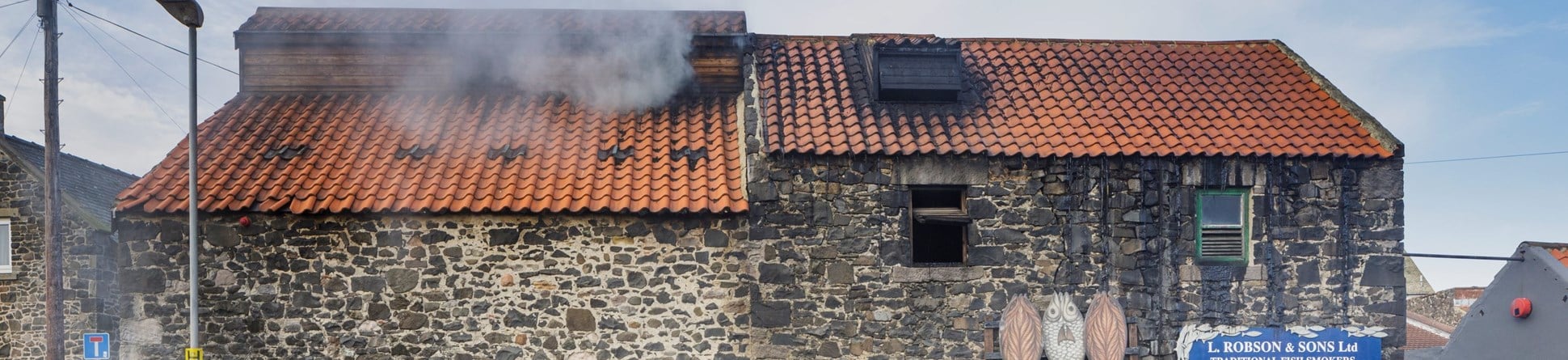 A stone building next to a road with smoke coming out of the roof.