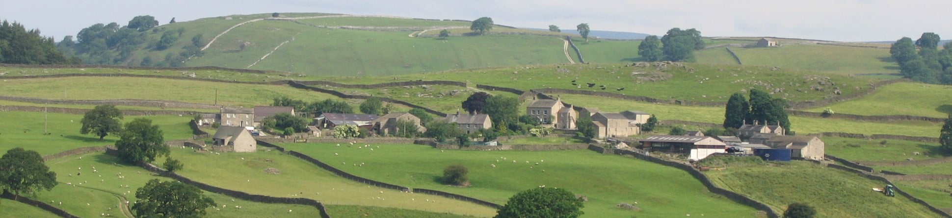 Village of Drebley in Yorkshire Dales National Park viewed from the SE across a river in the foreground.