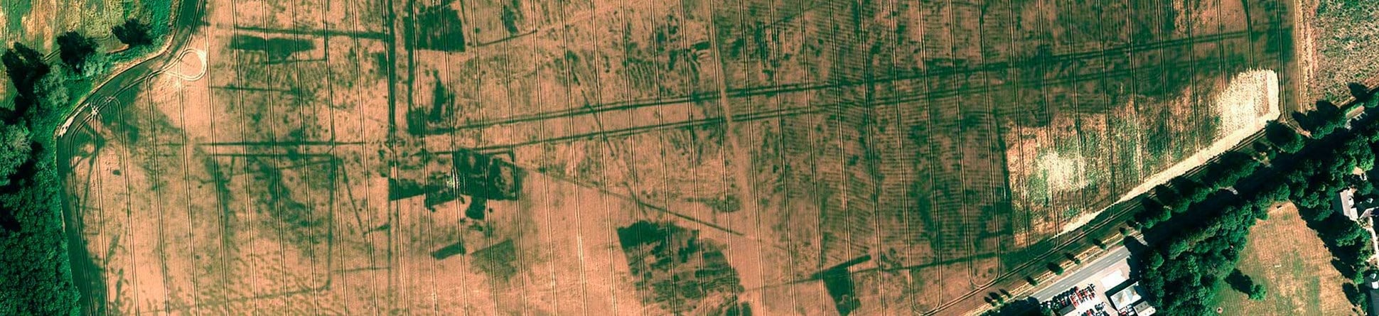 Colour vertical aerial photo showing an arable field with archaeology seen as darker green lines against a pale background