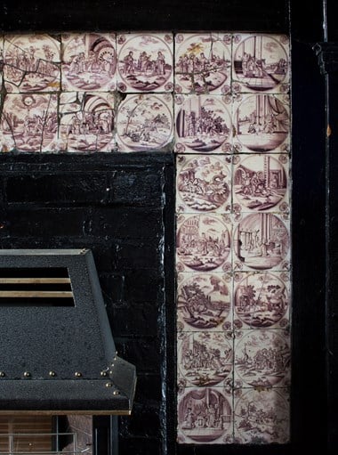 Tiles depicting a variety of scenes set into a black surround of a fireplace.