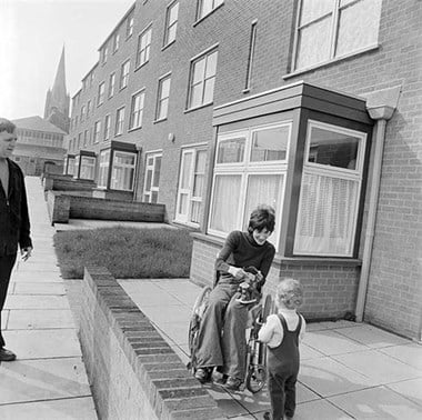 A woman in a wheelchair with a young child in front of 25 to 30 Whitby Court: a development of low rise accessibly designed flats and houses in Islington, London. 1977