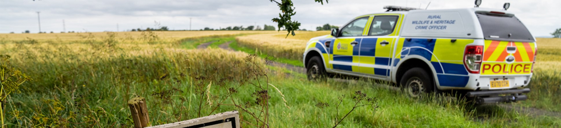 A photograph of a police SUV parked in a field. A sign in the foreground reads "Private Road / No entry"
