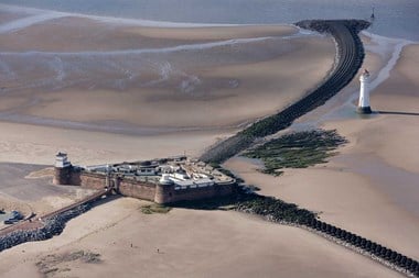 Colour aerial photo showing a brick built fort on the sands with stone embankments heading away from it towards the sea