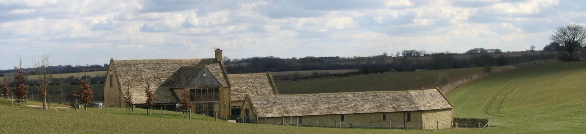 Stone farmhouse and building set in gently rolling landscape of fields of grass.
