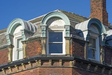 Three dormer windows on the corner of a red brick building.