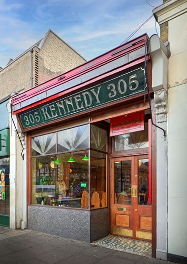 Outside the shopfront of the restored Kennedys Sausage Shop on Walworth Road. The large shopfront windows reflect the lights on inside the shop.