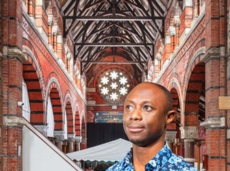 A man in a floral shirt stands in the nave of a brick-built church, the circular rose window behind him.