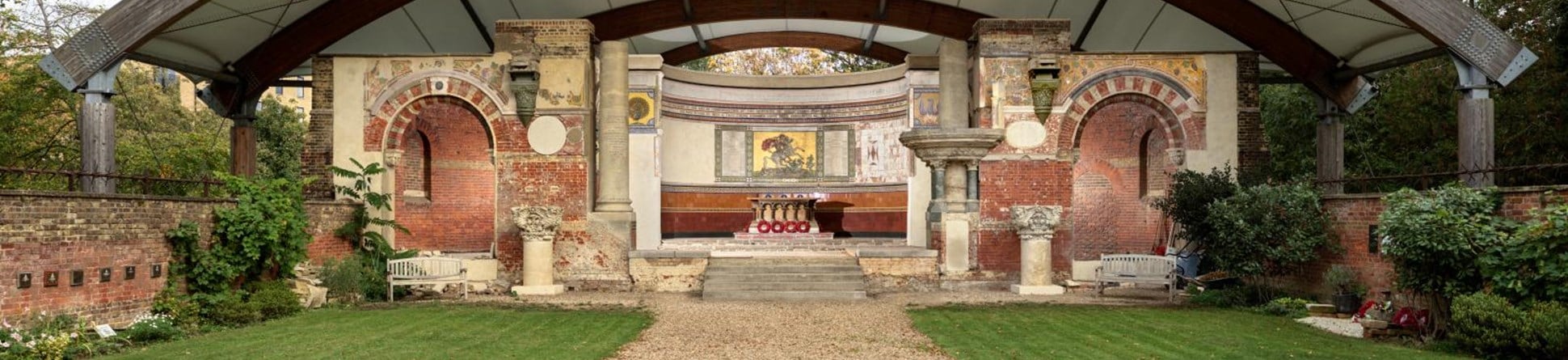 The altar, apse and end wall of a ruined church, all covered by a solid modern arched canopy