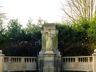 A statue of Florence Nightingale as the "lady with the lamp". The statue is raised on a pedestal and encircled by a larger monument. 