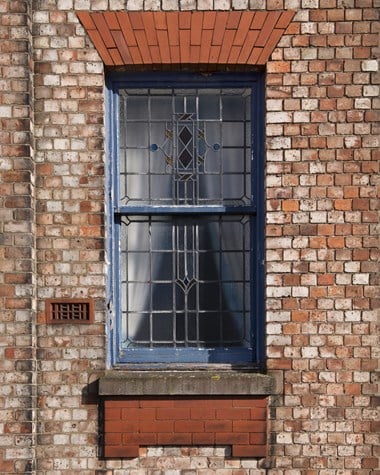 Sash window with stained glass set in brick building.