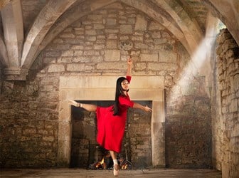 Dancer in red dress photographed in stone undercroft with vaulted ceiling.