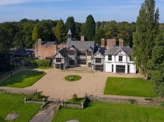 16th-century stately home with lawns and gravel in foreground. Woods in background.