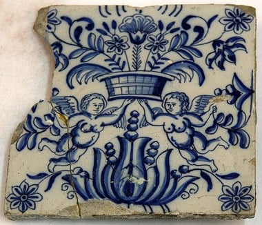A Dutch wall tile decorated with a smiling chubby winged puti beneath a basket of flowers dating to the 18th century. 