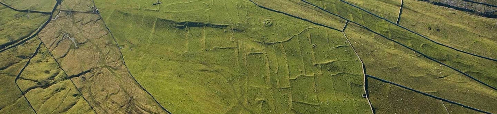 Colour aerial photo showing upland moors divided by dry stone walls with an underlying pattern of regular banks forming fields