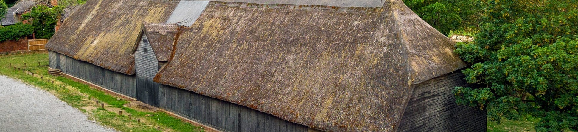 A weather-boarded aisled barn about 44m long and 11m wide. There is a gabled entrance in the centre of the north side. The thatched and half-hipped roof is of crown post construction with reversed assembly in the aisles.
