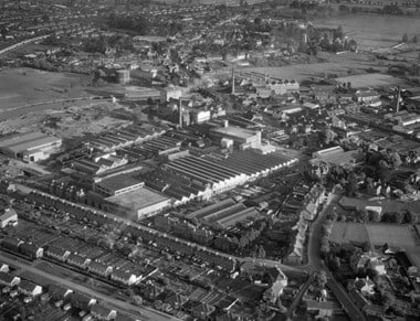 An aerial photograph of a large factory complex surrounded on three sides by streets with terraced and semi-detached housing and industrial buildings.