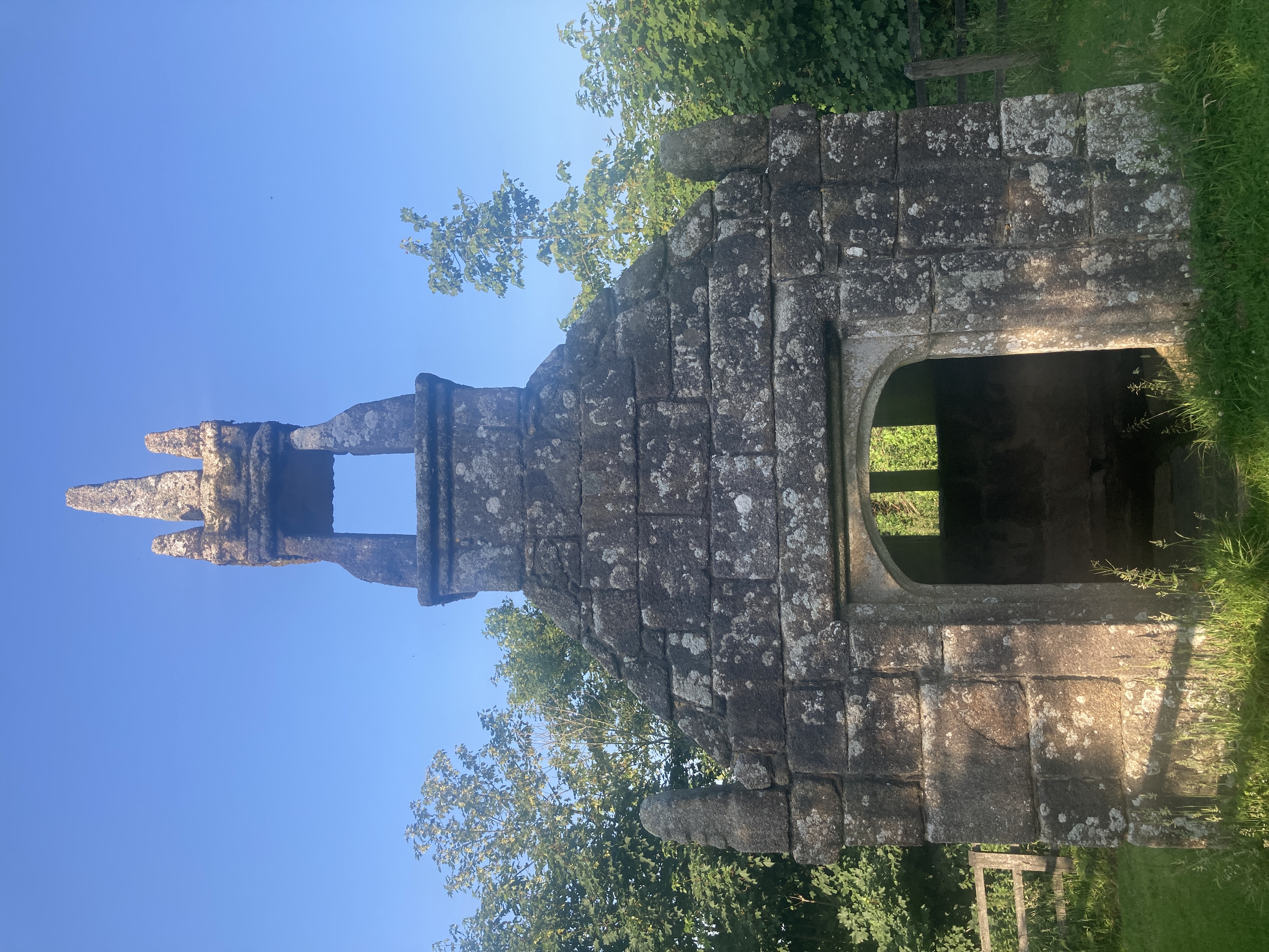 A small grey stone chapel with a tower on top and an open door showing the windows inside