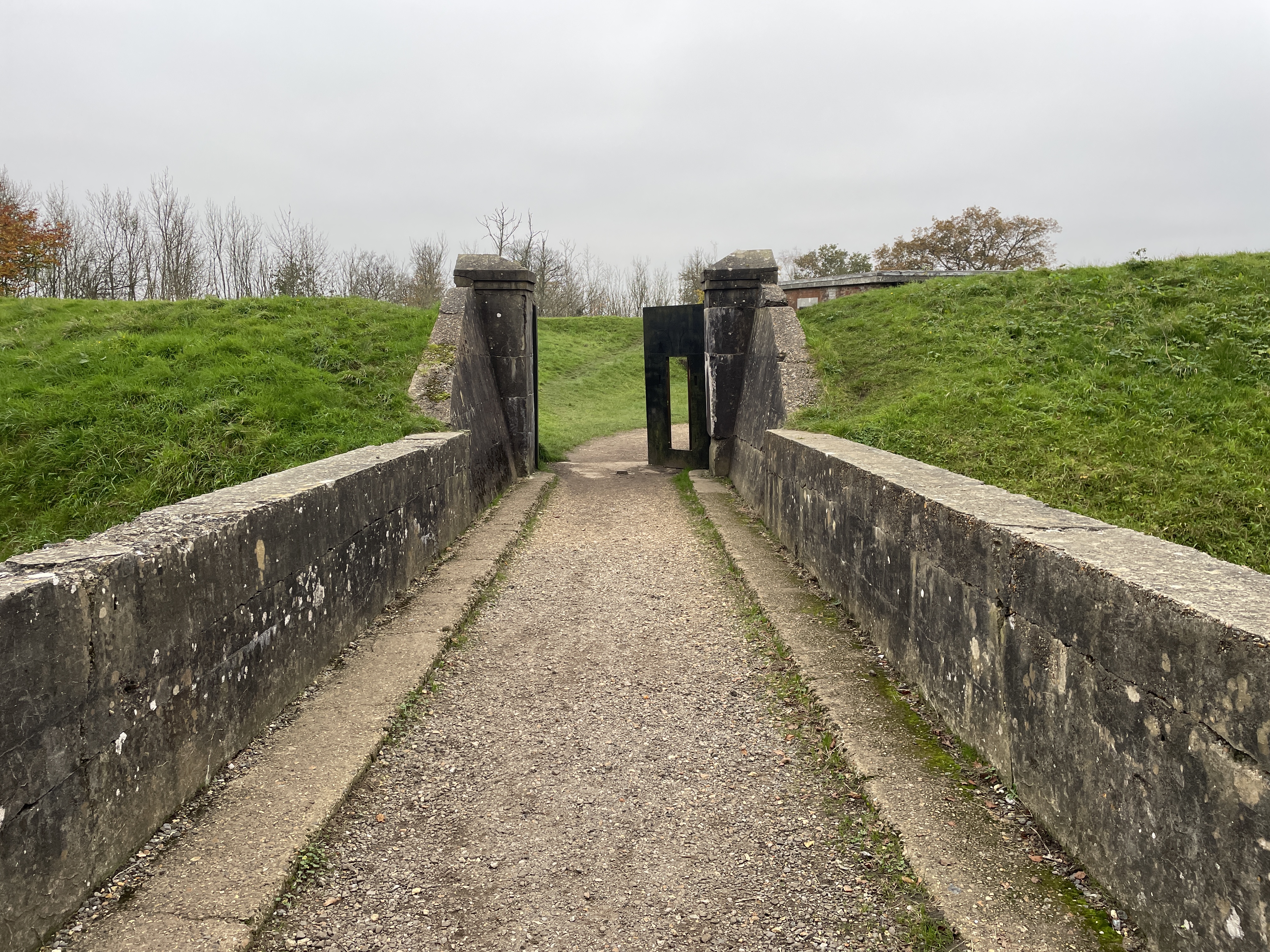 A track leading into a fort with earth ramparts and concrete entrance pillars