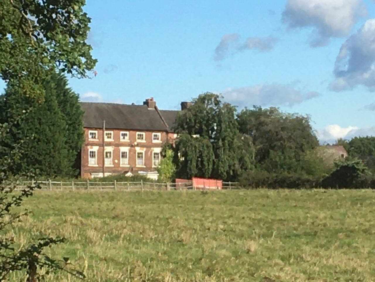 Photo of Yeildfields Hall Farmhouse from the Stafford Road, with house and outbuilding visible in the distance.