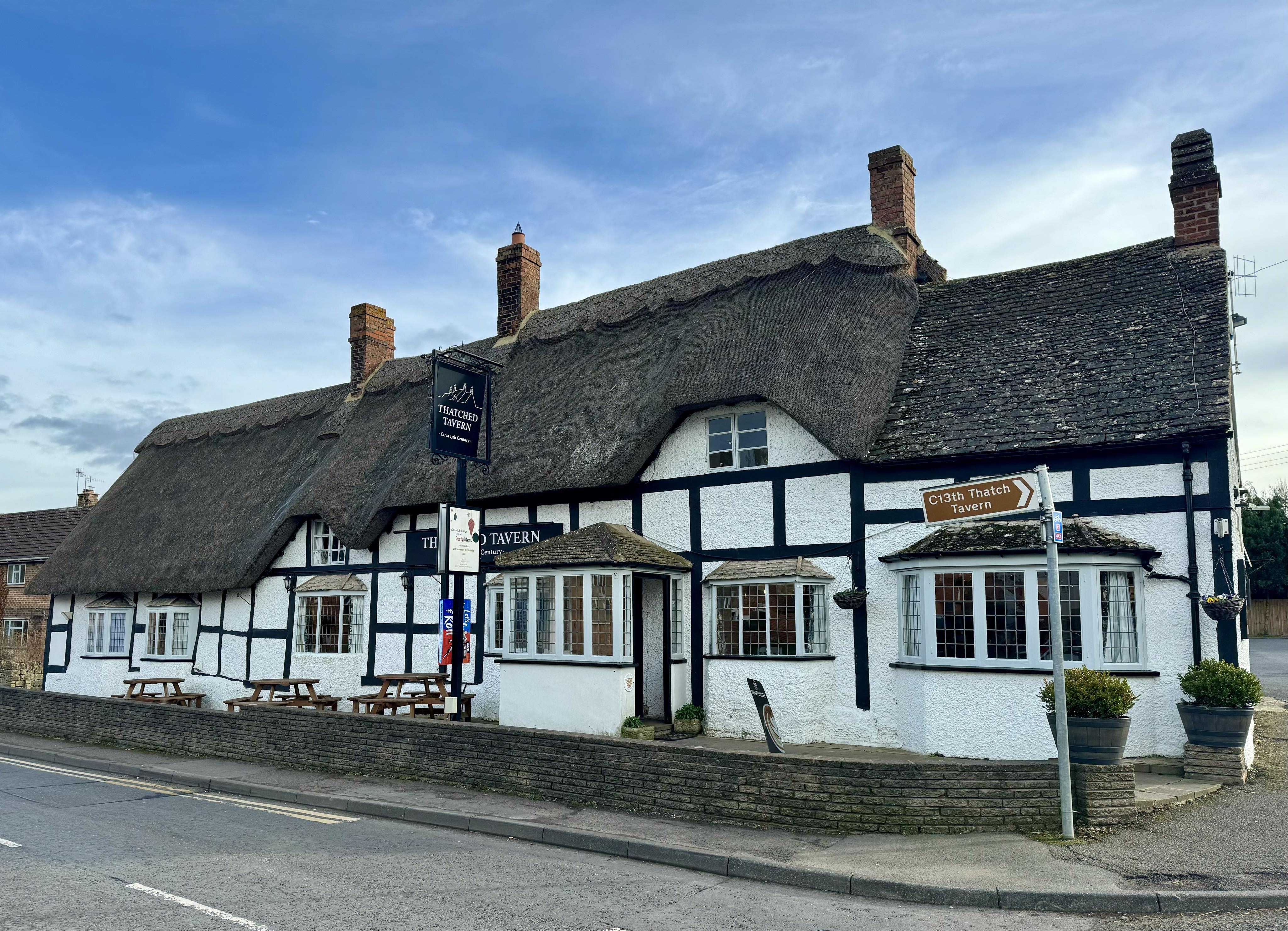 The long low street front  of the thatched pub showing the black timber framing and square white panels.