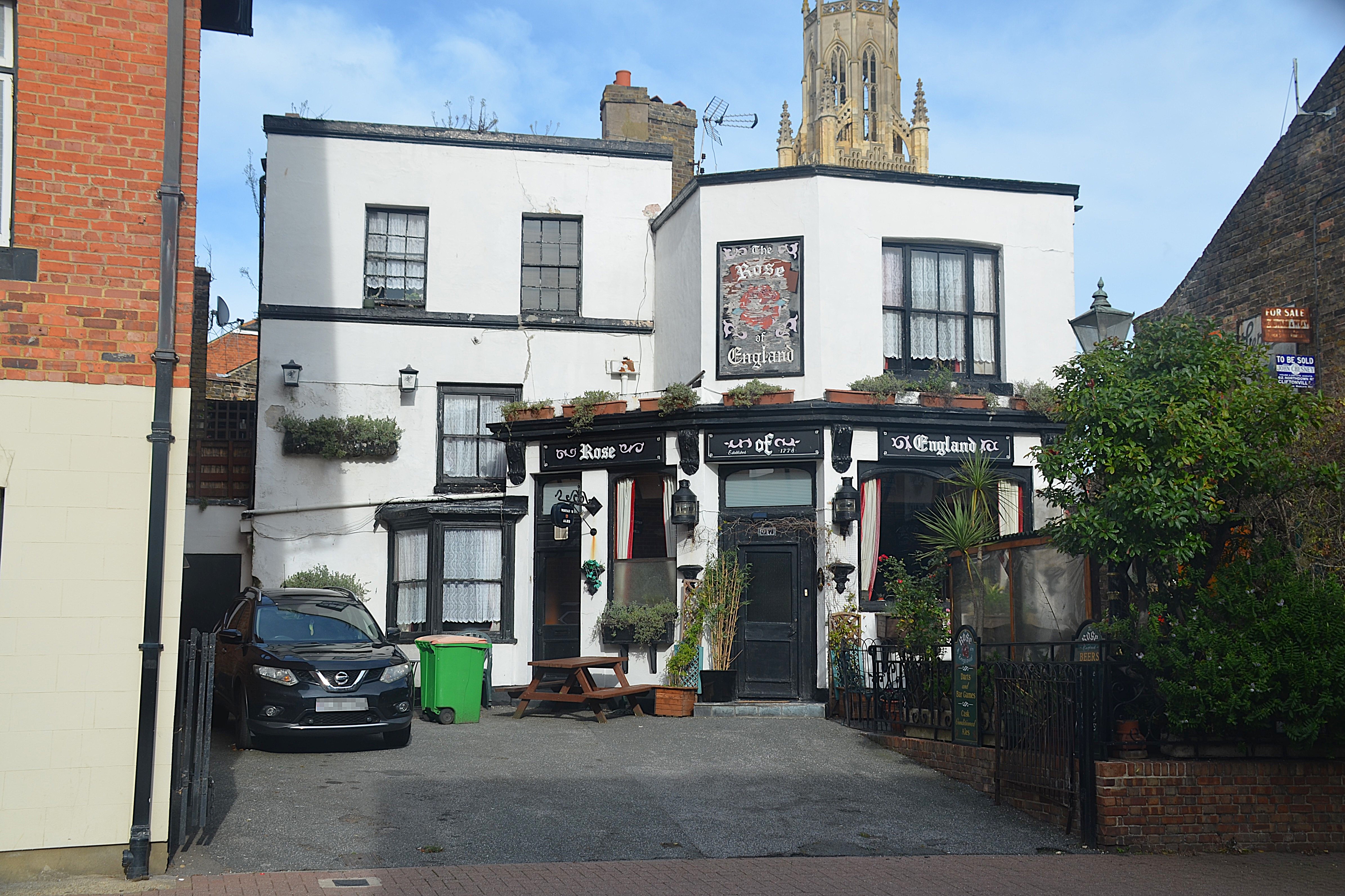 2/3-storey building with forecourt containing car on left, green bin and picnic table. Black-painted door to centre.