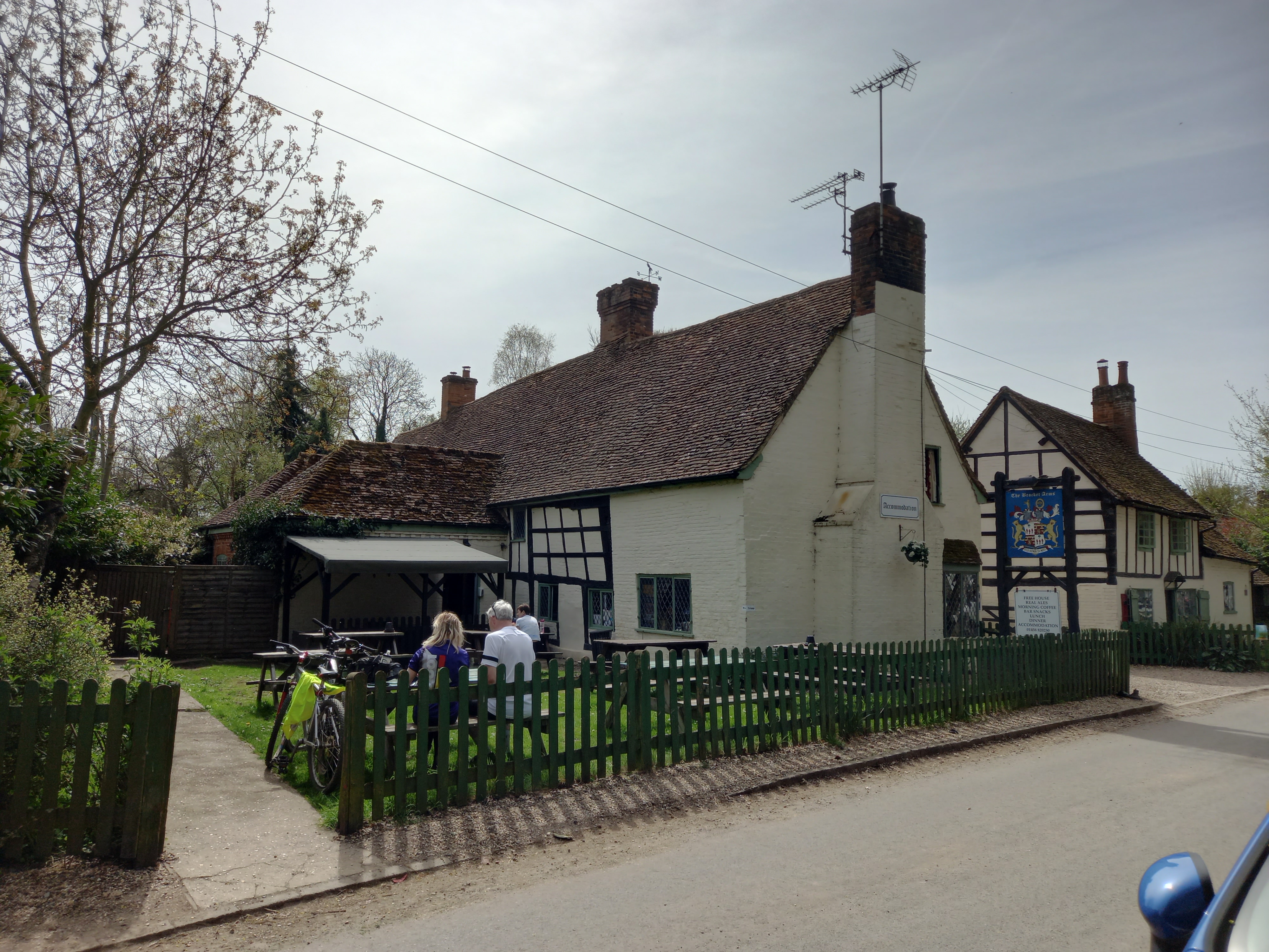 A long white building with a tiled roof and some central timber framing leaning at an angle. 