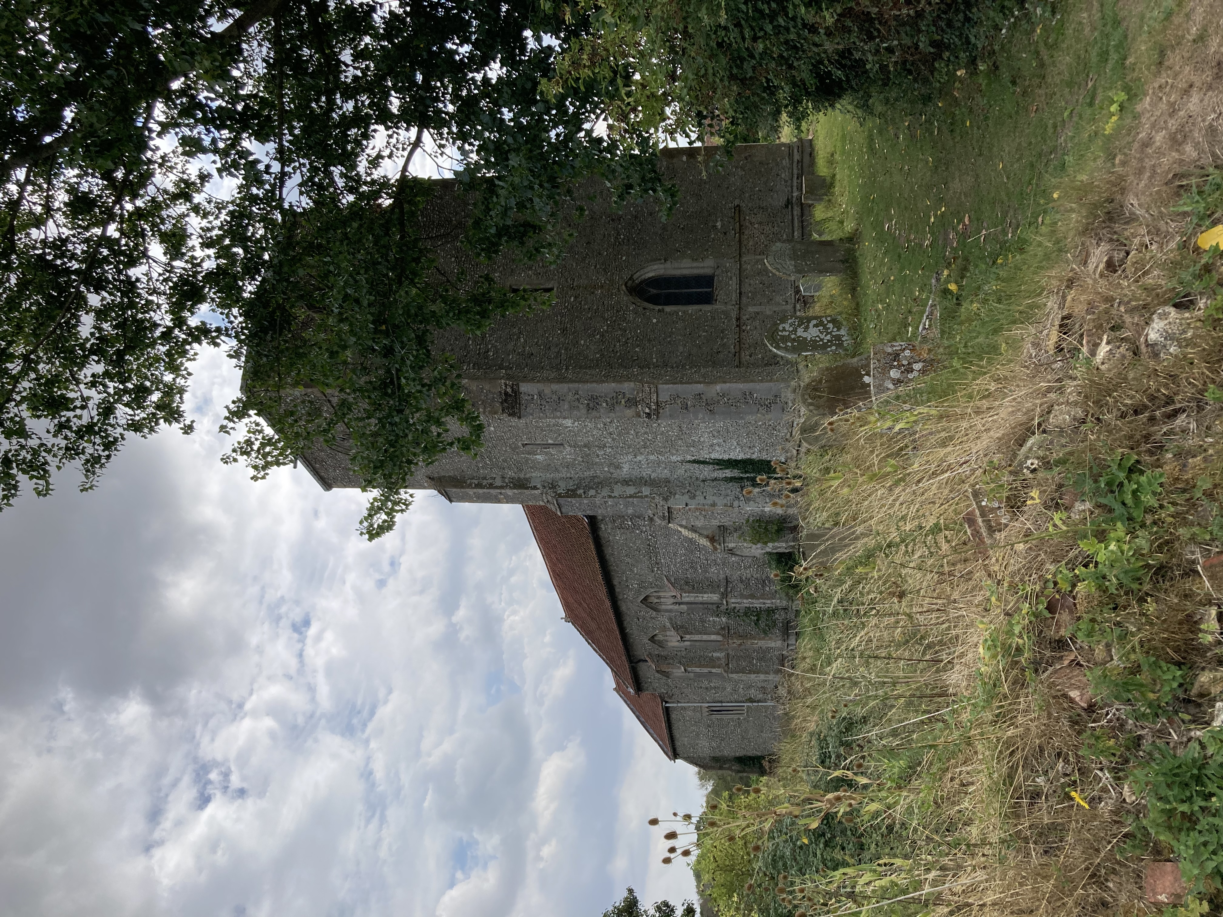 Church of St Peter, West Rudham - the west tower from the NW. A short church tower in flint with stone quoins.