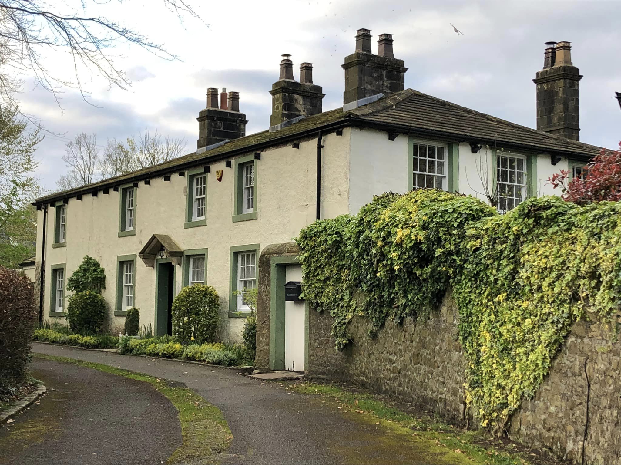 Beechthorpe is a cream painted house with green painted window & door lintels, on a curved road with bushes outside