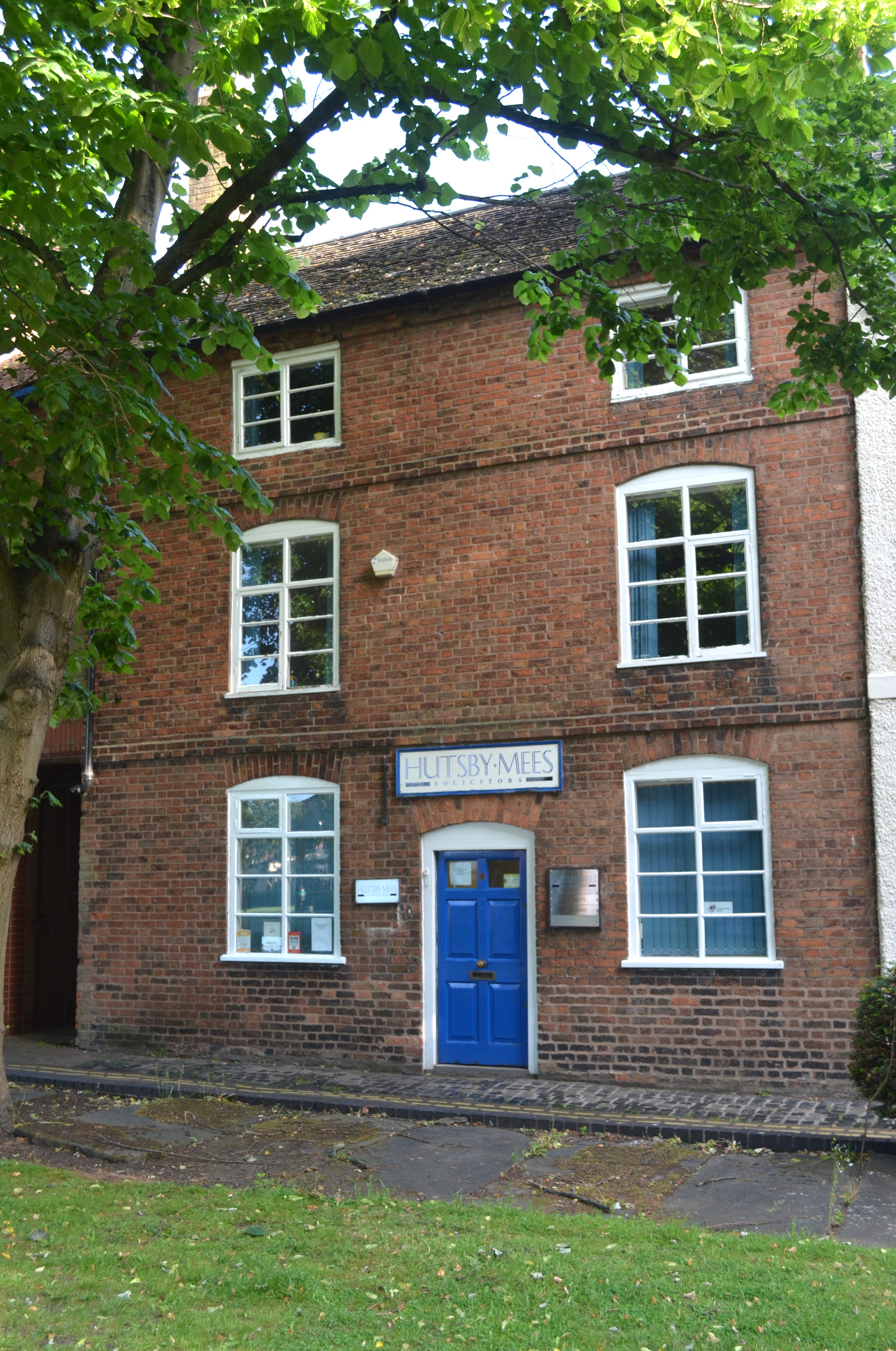 Three-storey building, with blue painted door in centre. Tree in leaf to left and top