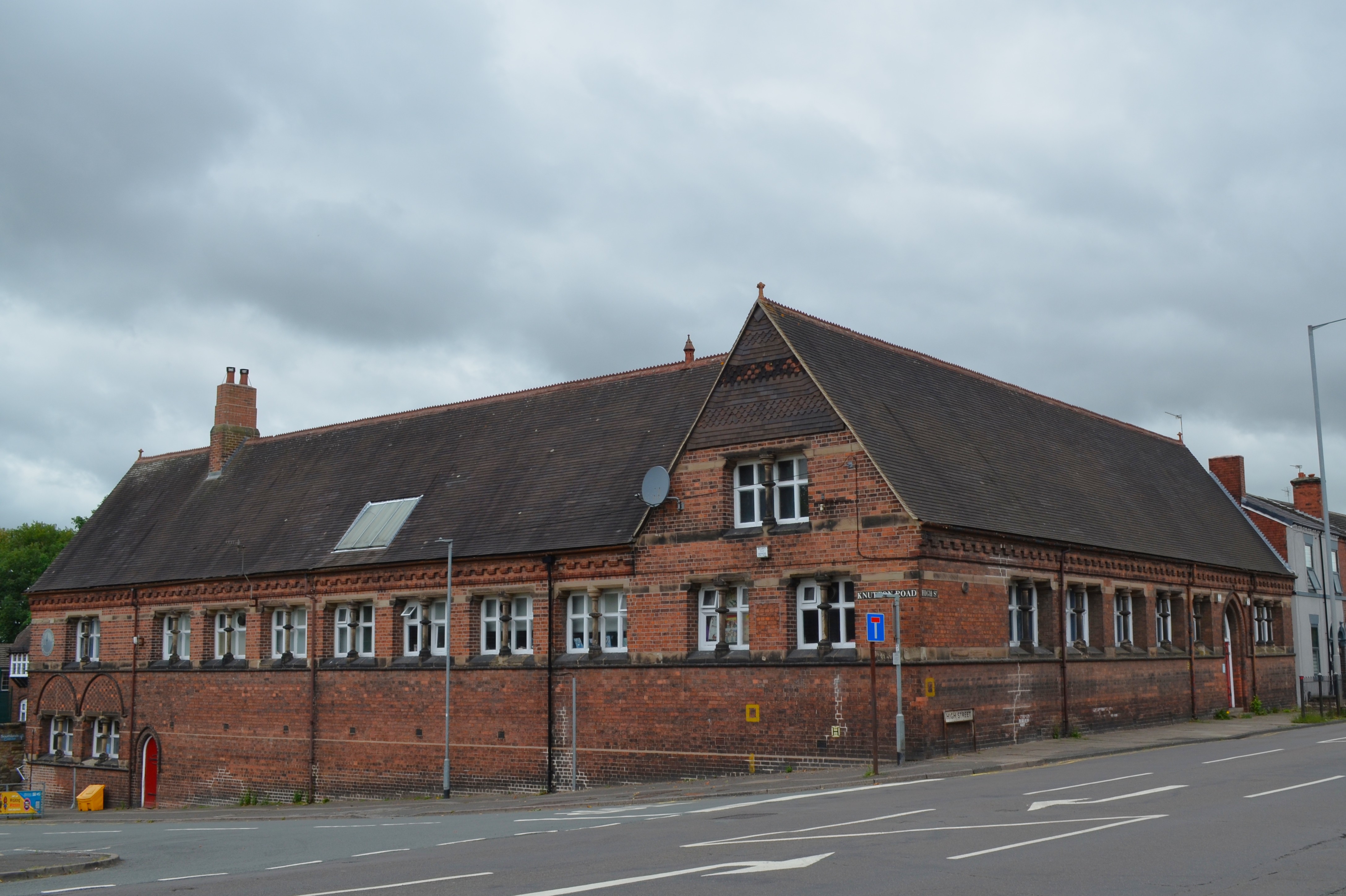 Single storey on High St to right. Knutton Rd on left slopes down giving a lower floor with red door. Yellow salt bin.