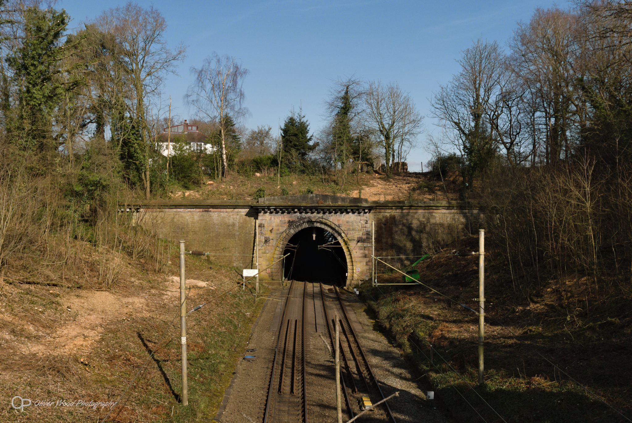 A photo of a railway tunnel in a deep cutting with blue sky and trees
