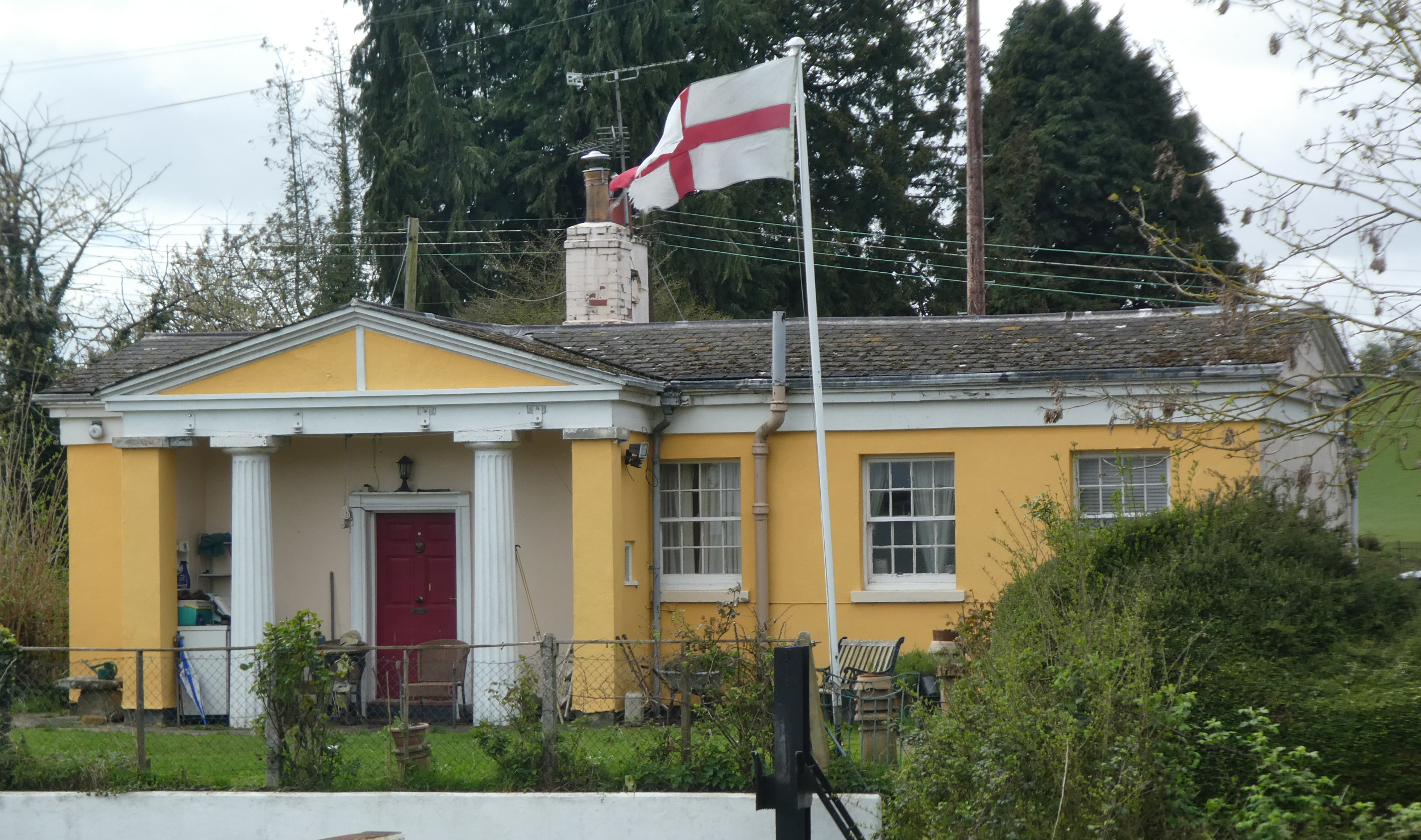 Yellow-painted, one-storey building, with classical columns and portico.
A St George's flag flies from a flagpole.