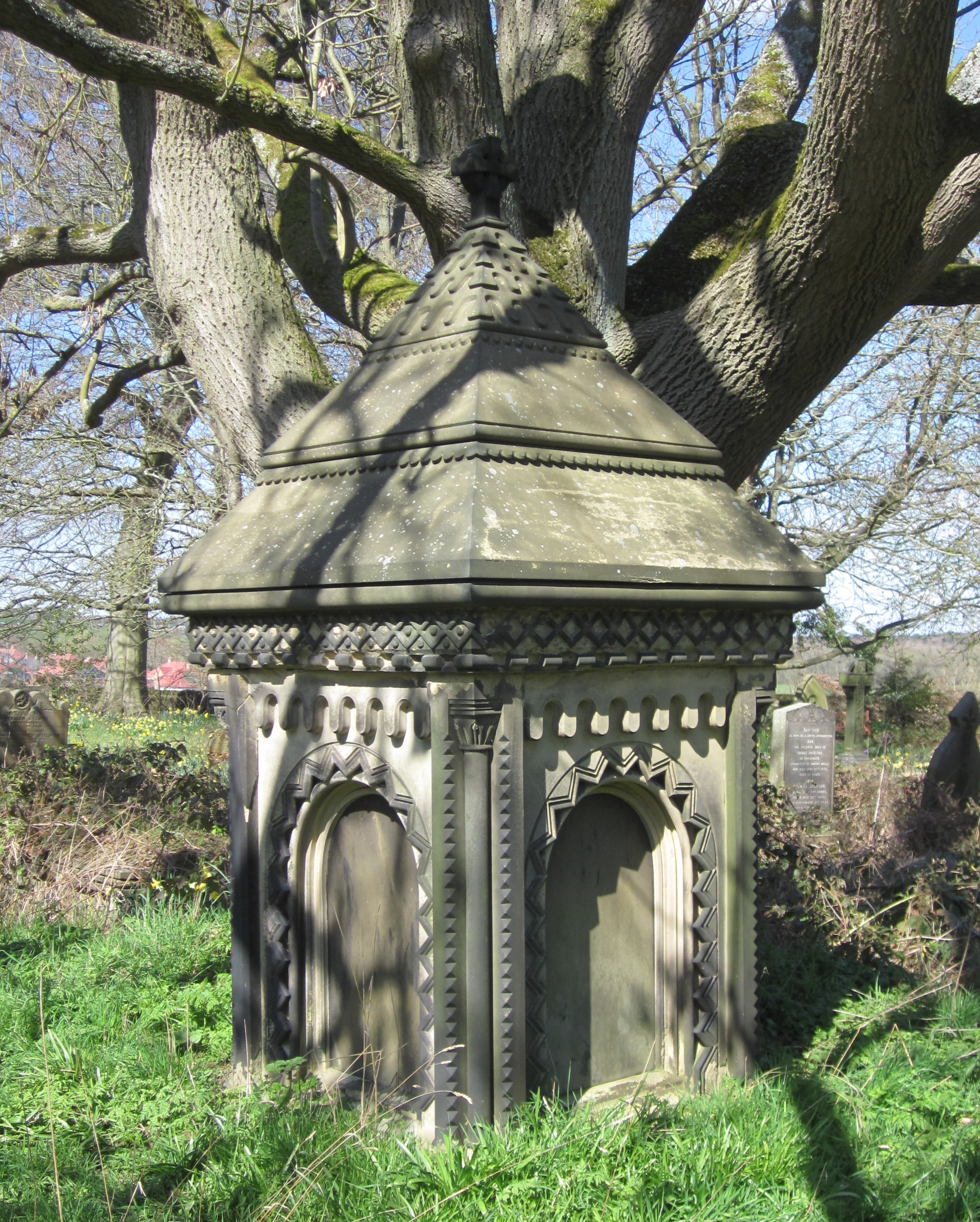 Square conical roof stone memorial in front of large tree.
