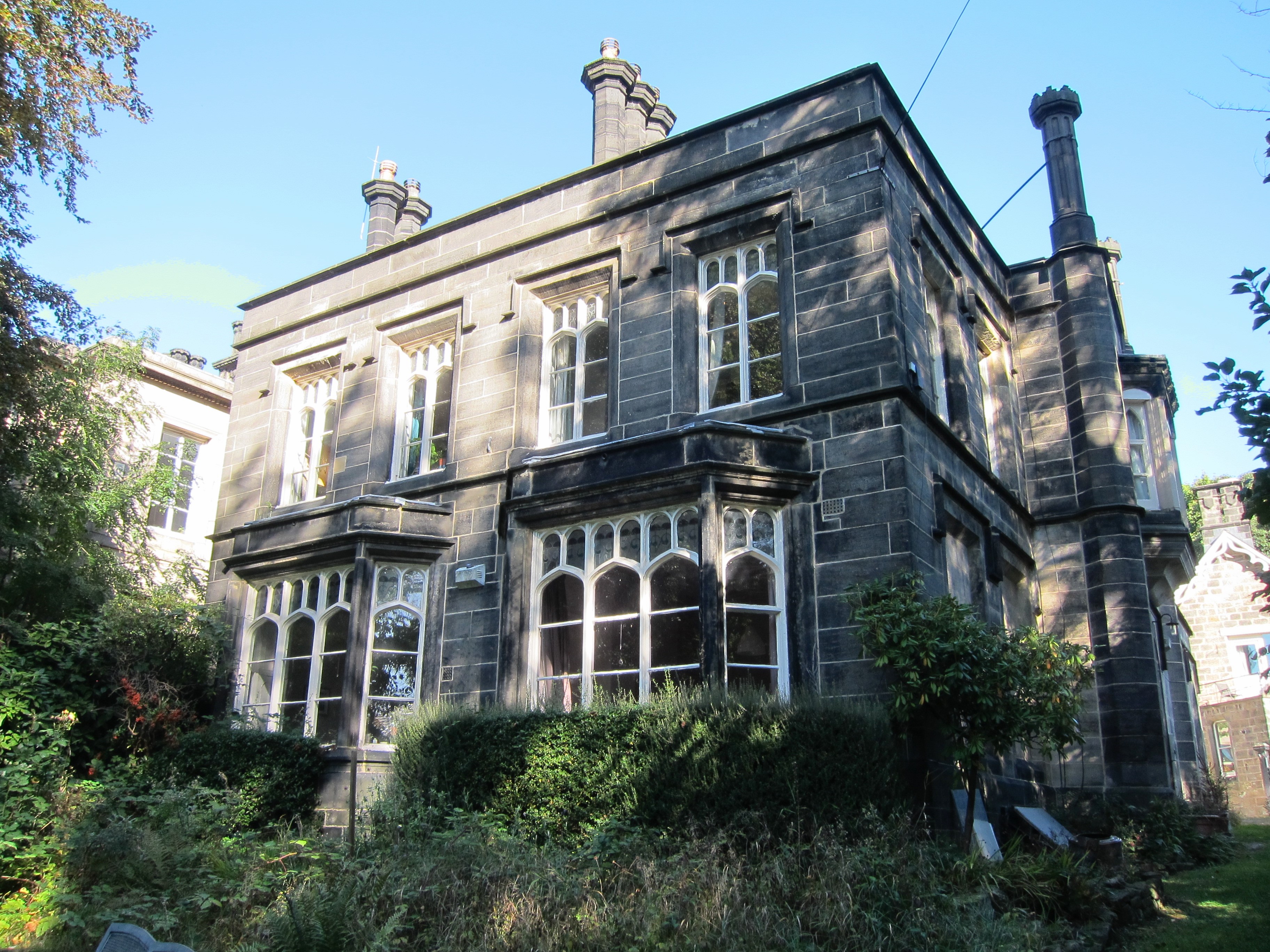 Stone two-storey building with two bay windows on ground floor, four above.  Two sets of chimneys.
