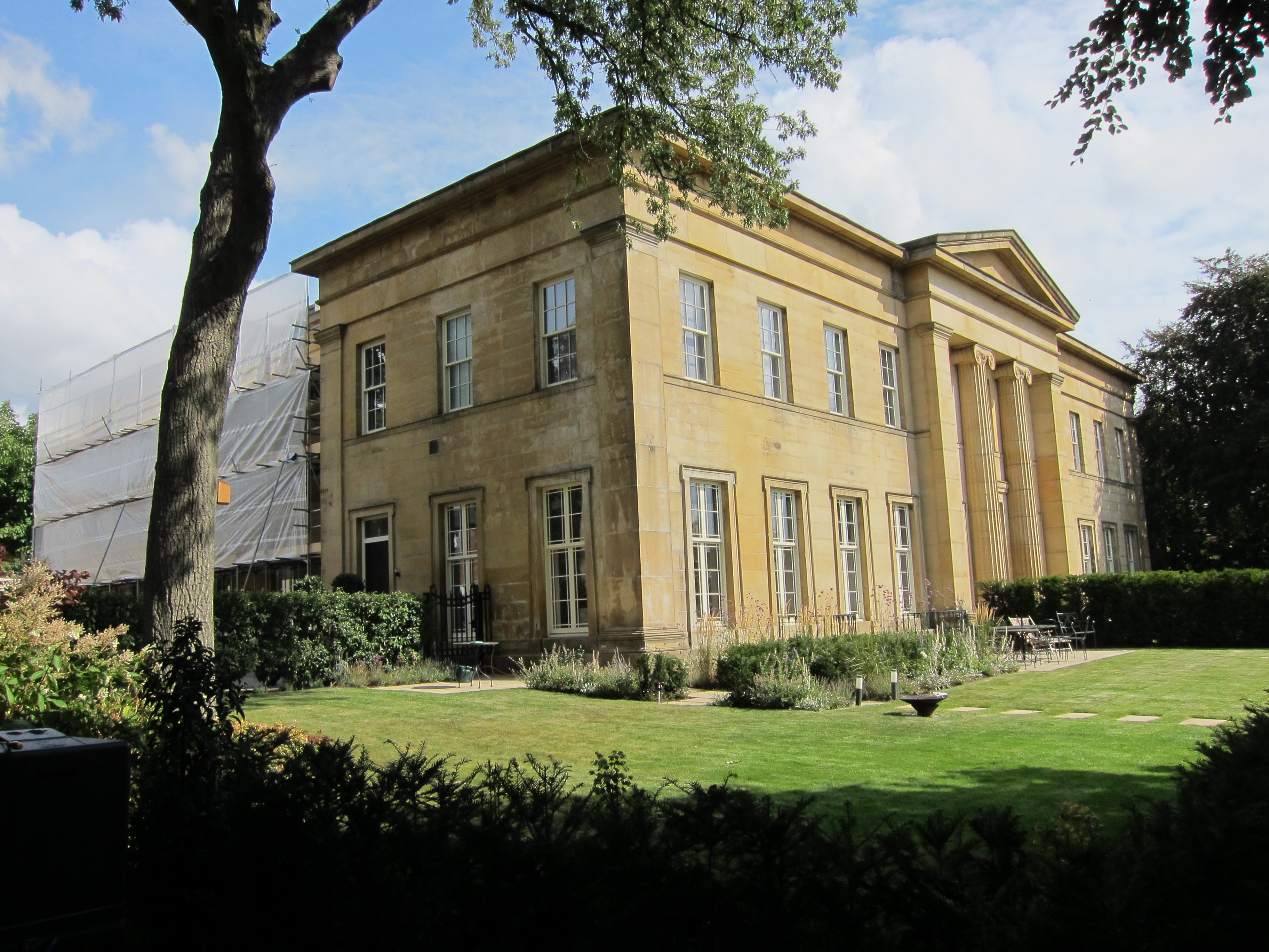 Corner view of 2 storey yellow sandstone building.  Right is front face with columns on portico.