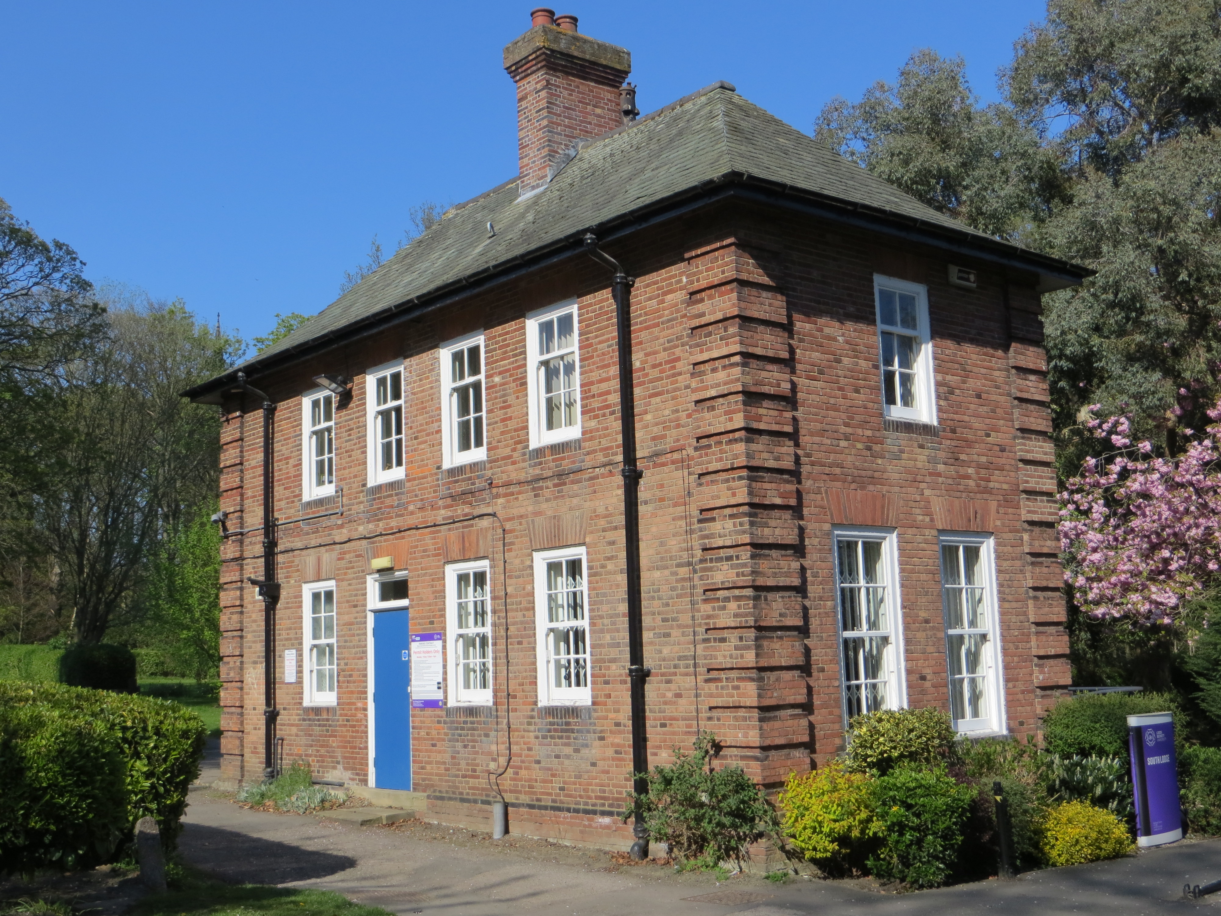 Corner view of two-storey brick house with chimneystack.  4 front windows on first floor, 3 plus blue door on ground. 