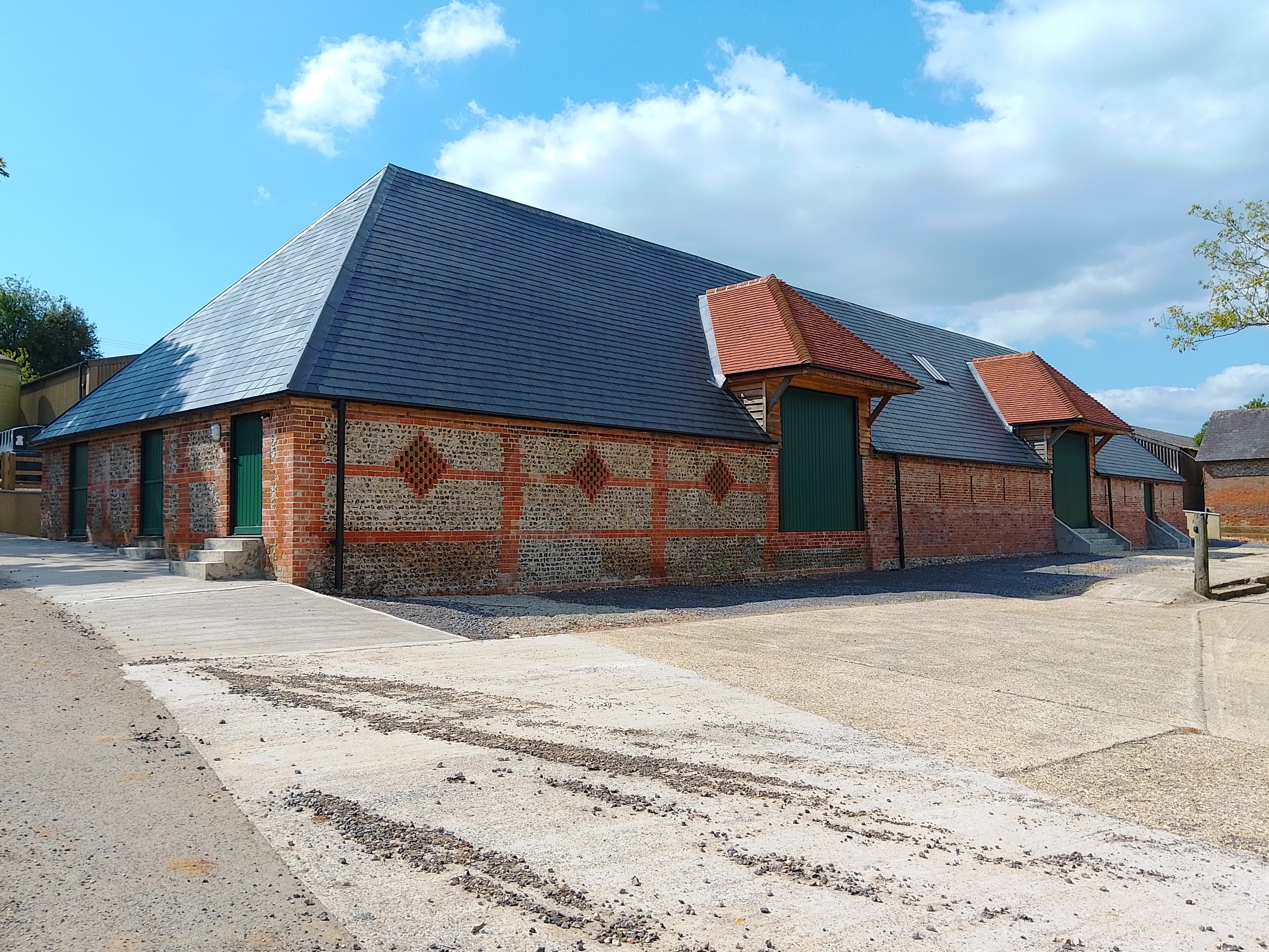 A rectangular barn front: brick walls with flint dressings and grey tile roof. Two large doors and two small to side.
