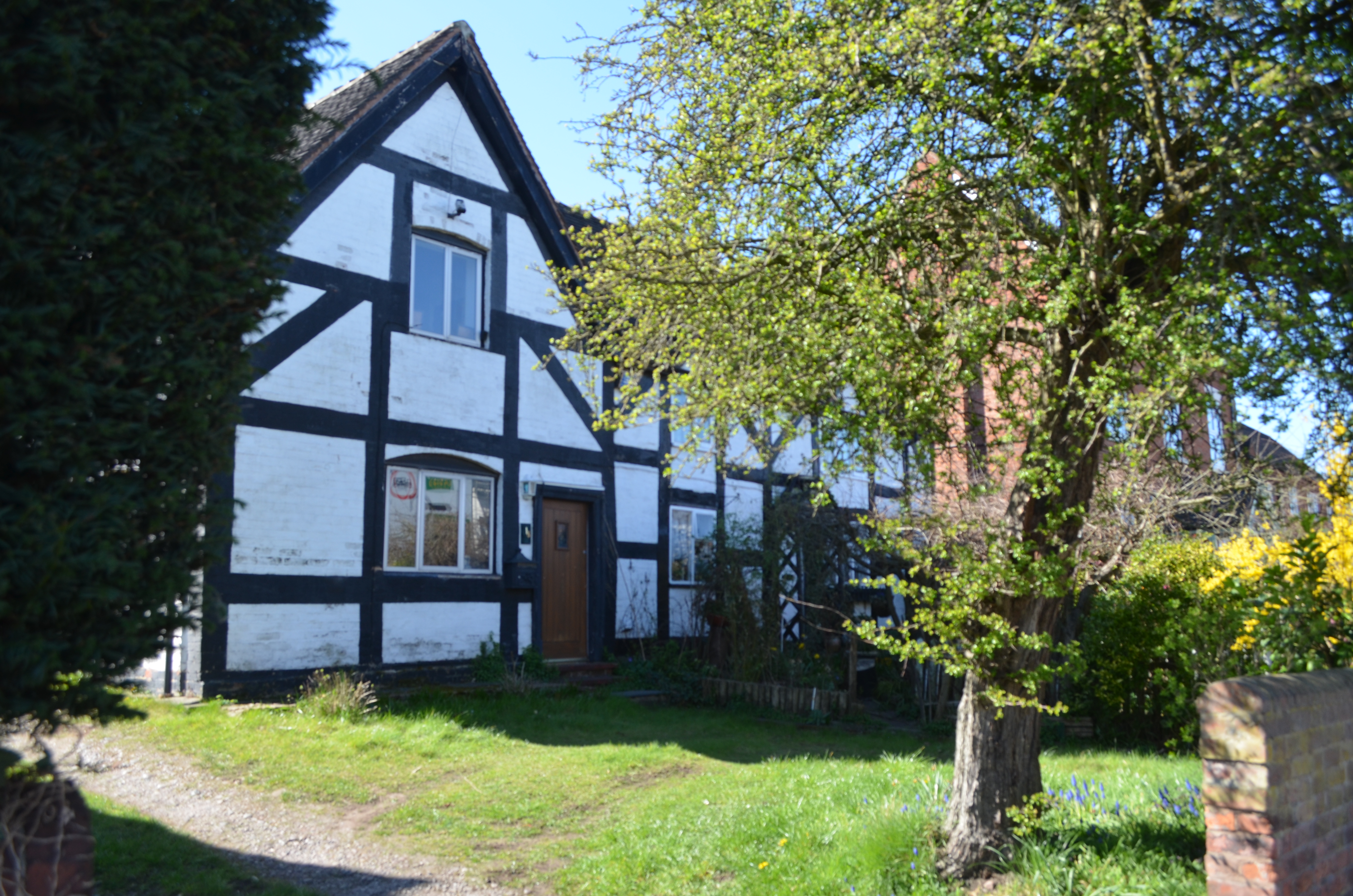 Black and white timber-framed house with front grassed area. No 16 is just visible behind the tree foliage on the right.