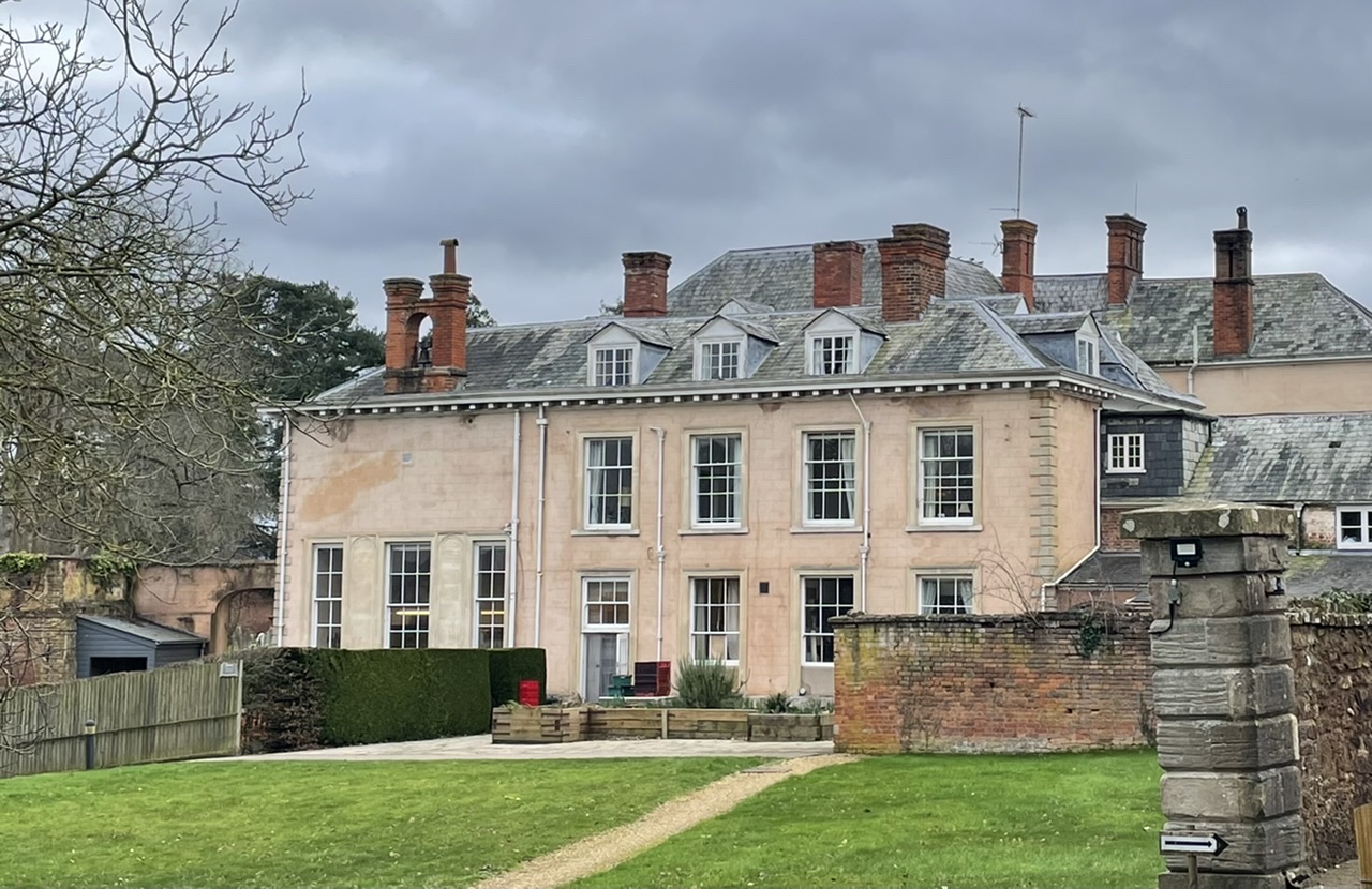 Country house - pink/peach finish wall. 3 tall windows on left section. 2 rows of windows on main section with 3 dormer