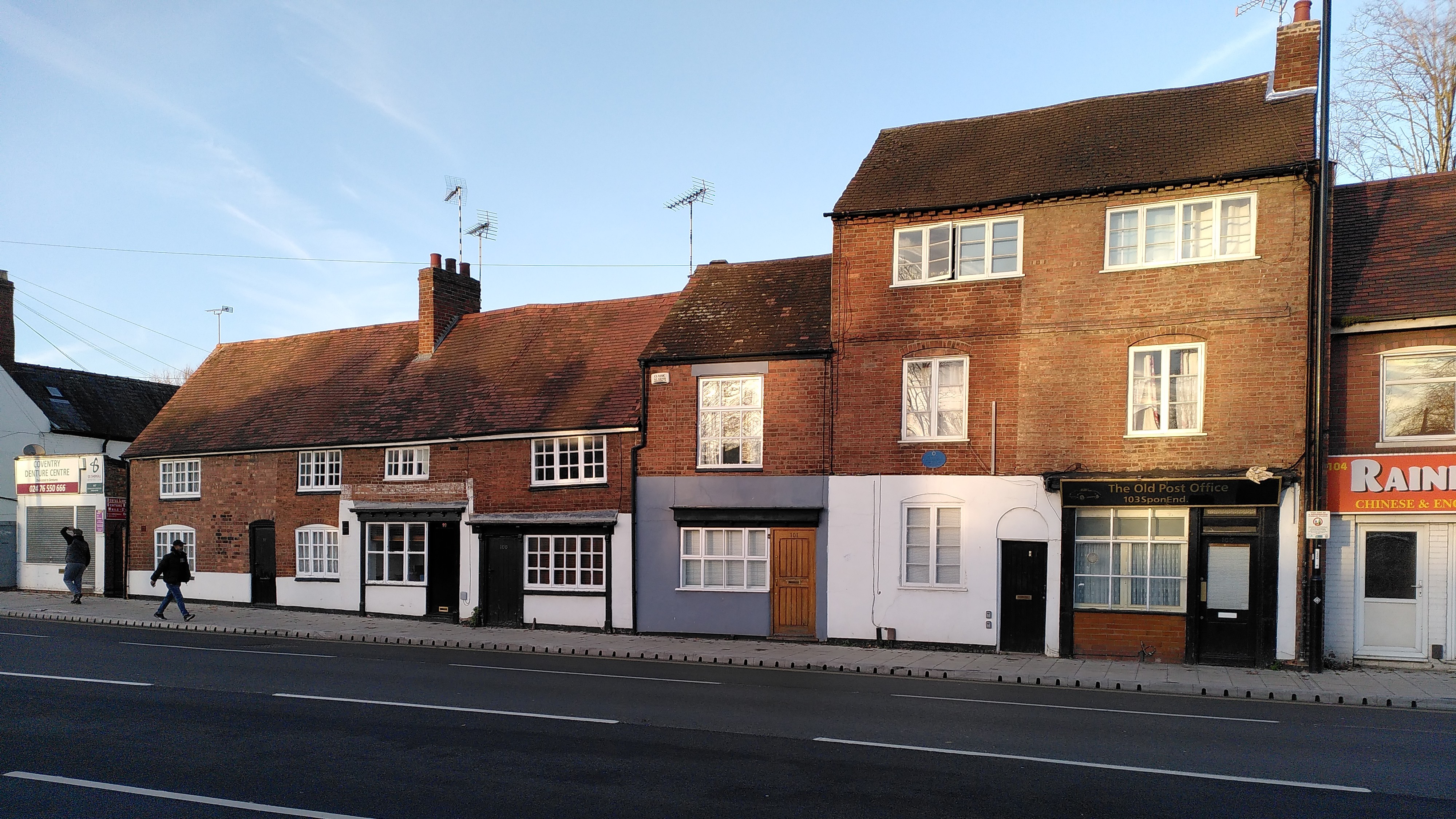 A row of two and three storey vernacular houses with red brick fronts, some with shop fronts.