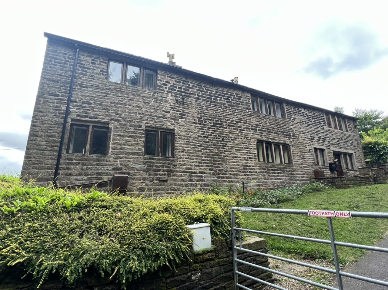 The stone building is above the road level, on a steep slope. Small windows sit spread out on the wall. 