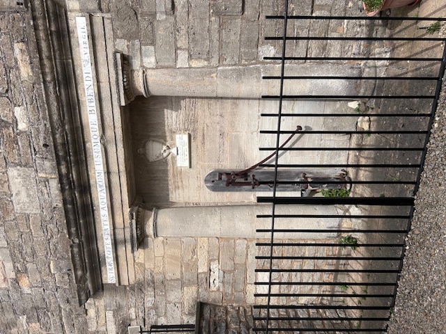 An old spa pump on the side of a building set behind black iron railings.