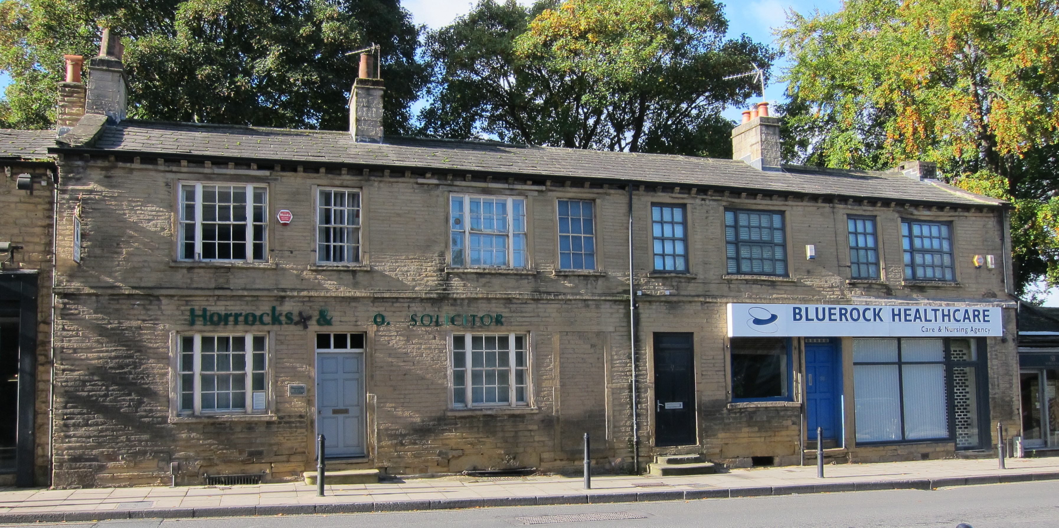 Two storey stone row of houses with square pane windows, except ground floor right shop window style.