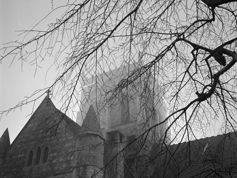 Looking up at the north transept and central tower of St James' Church, seen at night through the branches of a winter tree