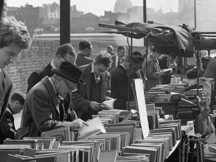 Men browsing at a second hand book stall on Farringdon Road, with the dome of St Paul's Cathedral visible in the distance