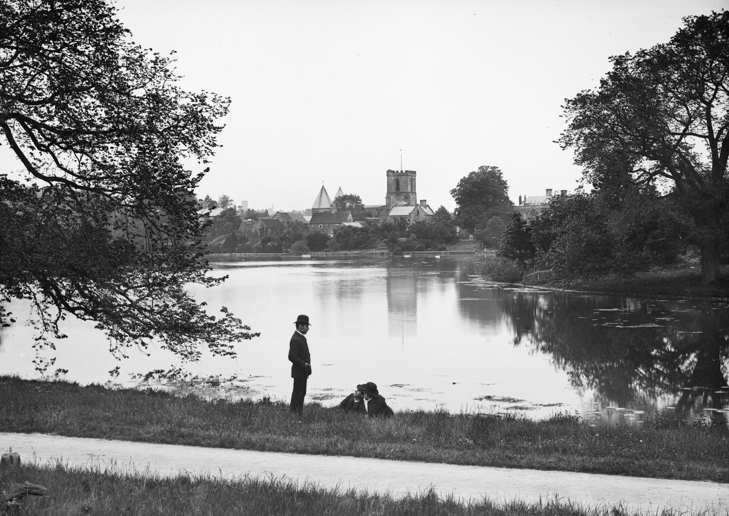 /localA historic photograph with churches across a body of water and three people in the foreground