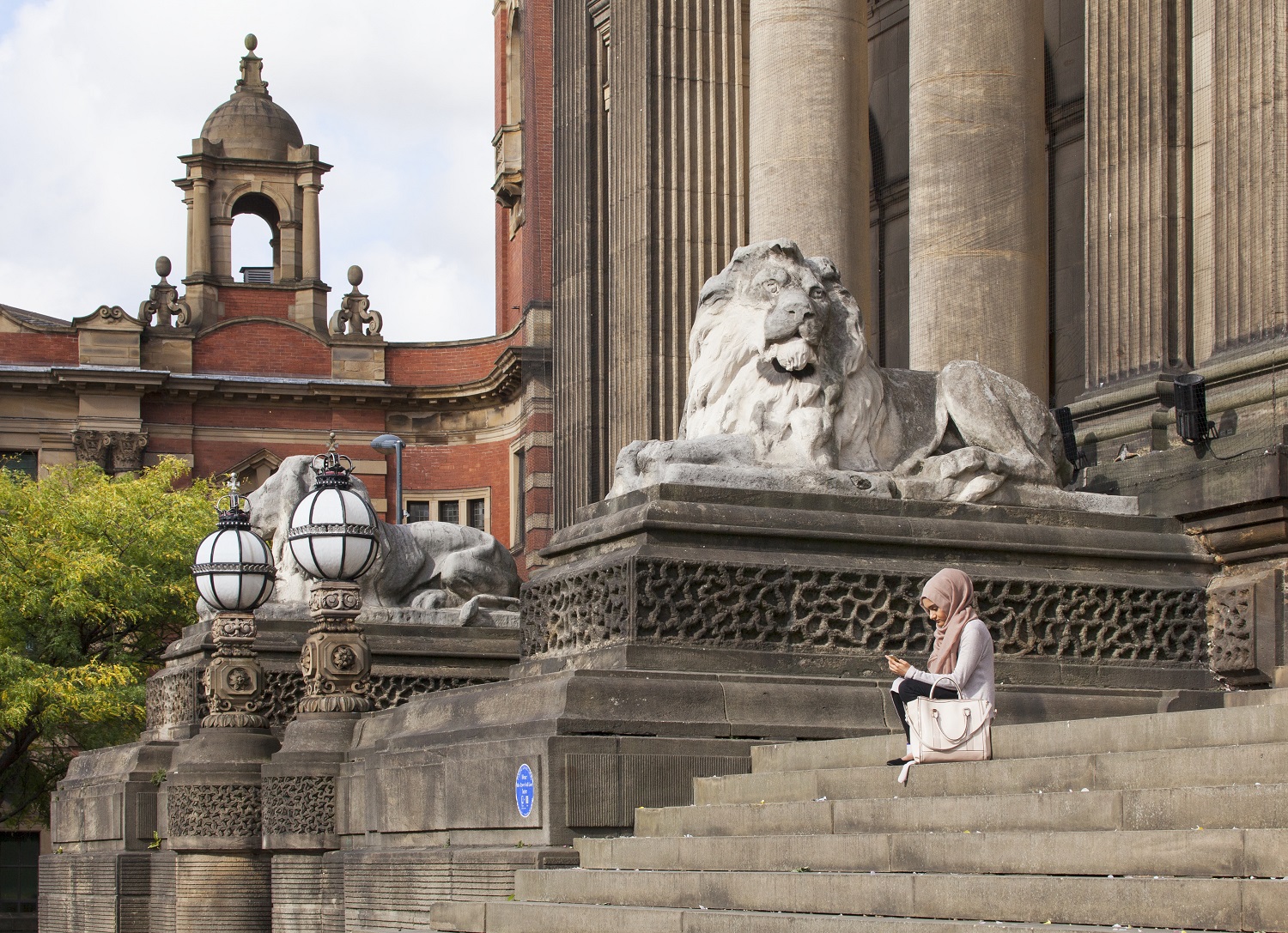 /localA woman sitting on the steps of the Town Hall, with a lion sculpture and columns in the background