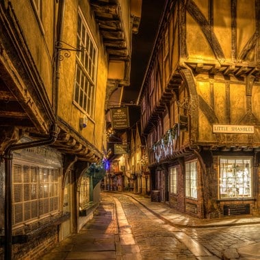 A nighttime photograph of a narrow-cobbled street lined with medieval buildings.