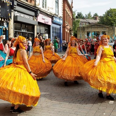 Dancers at a street carnival wearing bright yellow hoop dresses